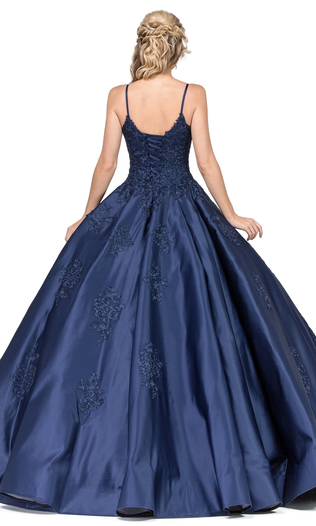 A woman with braided blonde hair models the Quinceanera Dress 1325 by Dancing Queen, a navy blue sleeveless A-line ball gown with lace applique, shown from the back against a white background.