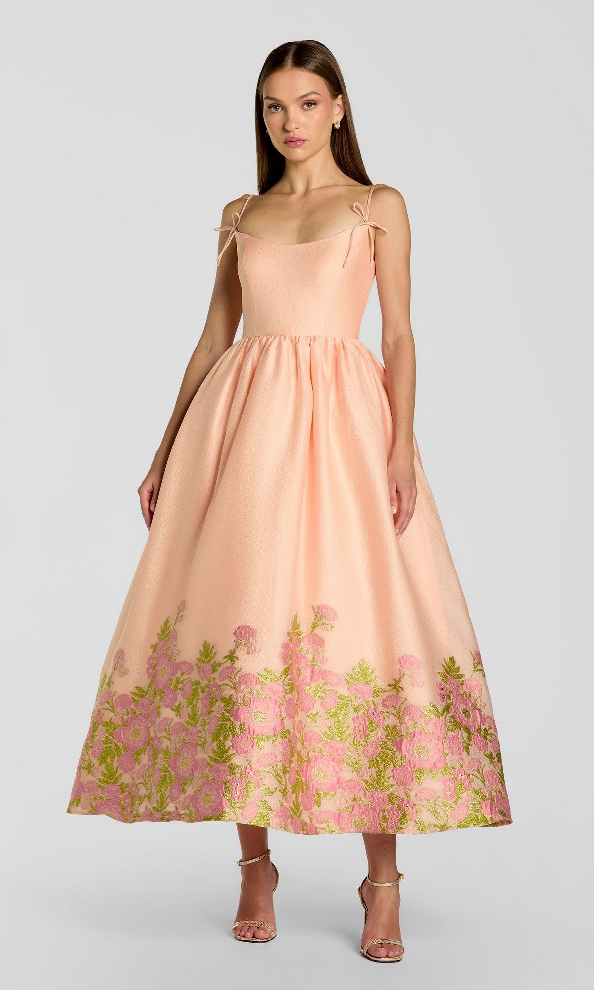 A woman wearing the Tea-Length Party Dress: Mac Duggal 13266 in Pink Multi, featuring floral embroidery at the hem, poses against a plain light background.