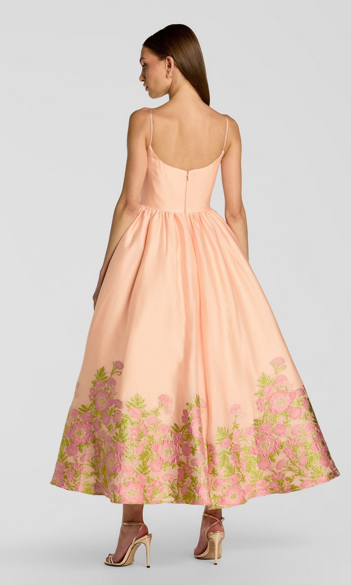 Against a plain background, a woman is seen from behind wearing the Mac Duggal 13266 tea-length party dress in peach, featuring organza fabric with a flared skirt and a delicately floral-embroidered hem. She pairs the dress with beige high-heeled sandals.