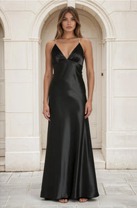 Woman wearing a black satin gown standing in front of a stone archway.