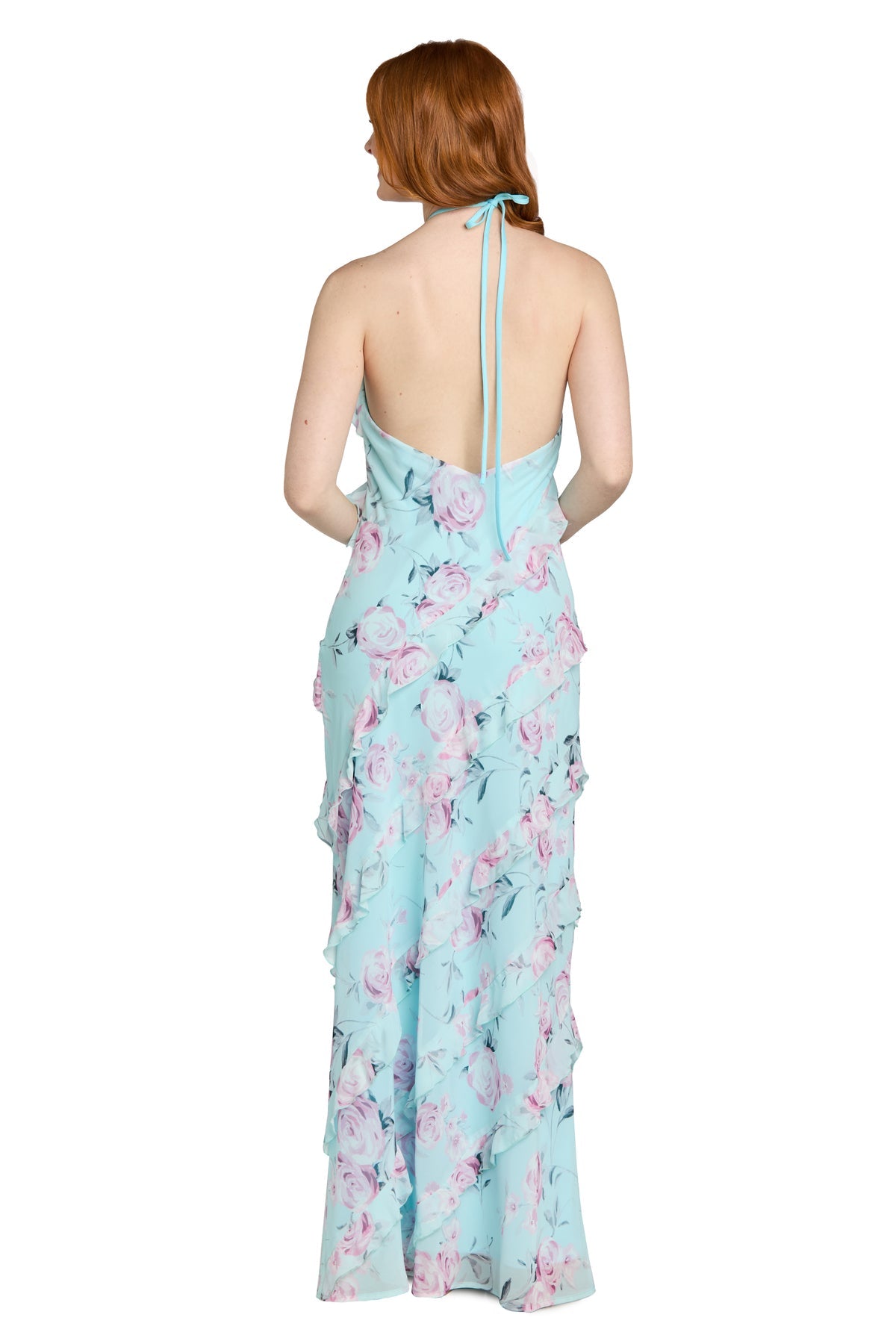 A woman with red hair is standing and facing away from the camera, wearing the Floral Ruffled Maxi Dress: Morgan 14173โa light blue maxi dress featuring a floral print, ruffle tiers, and an open back.