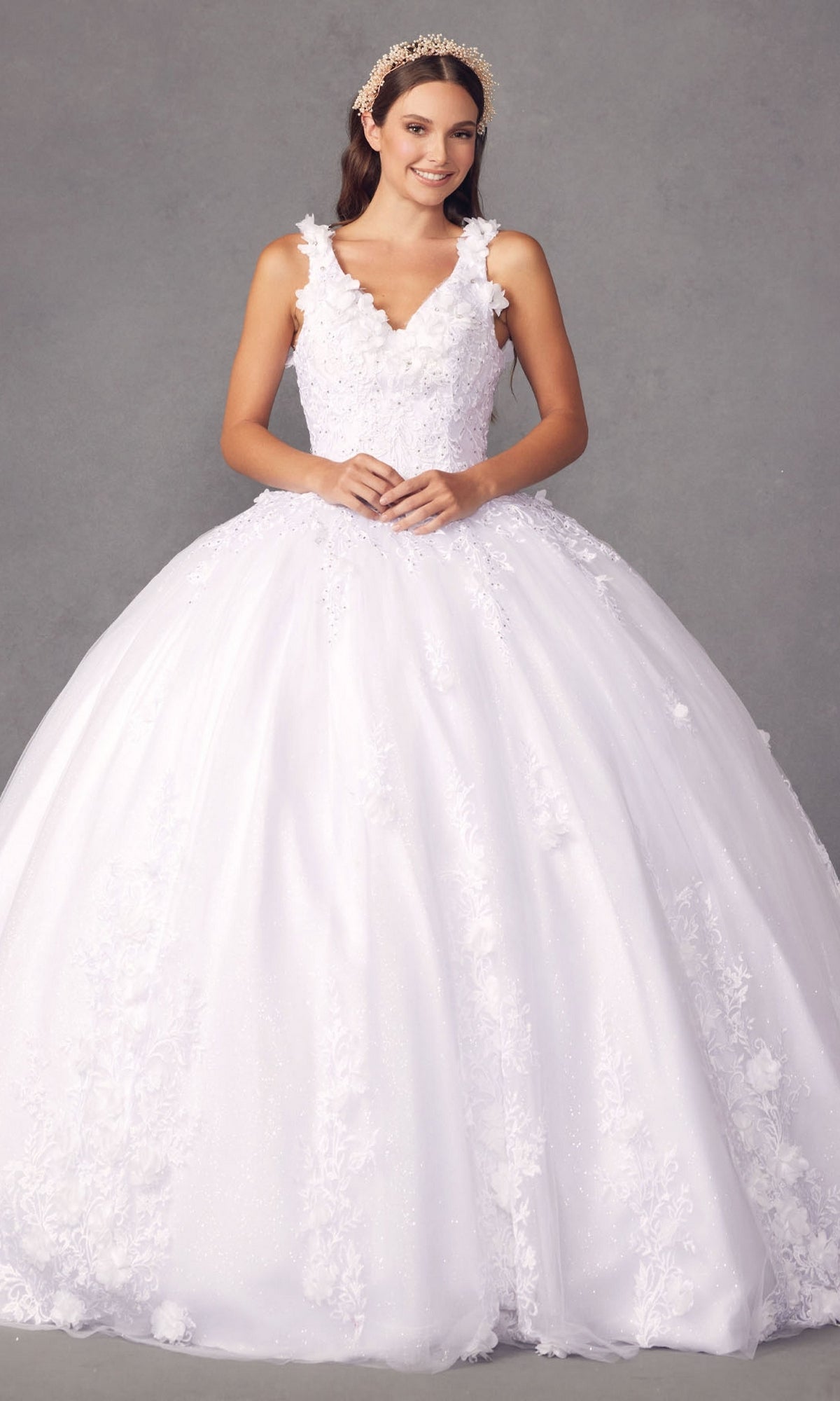 A woman smiles against a gray background, wearing the Juliet 1437W Traditional White Quinceañera Dress with floral appliques and a jeweled headband.