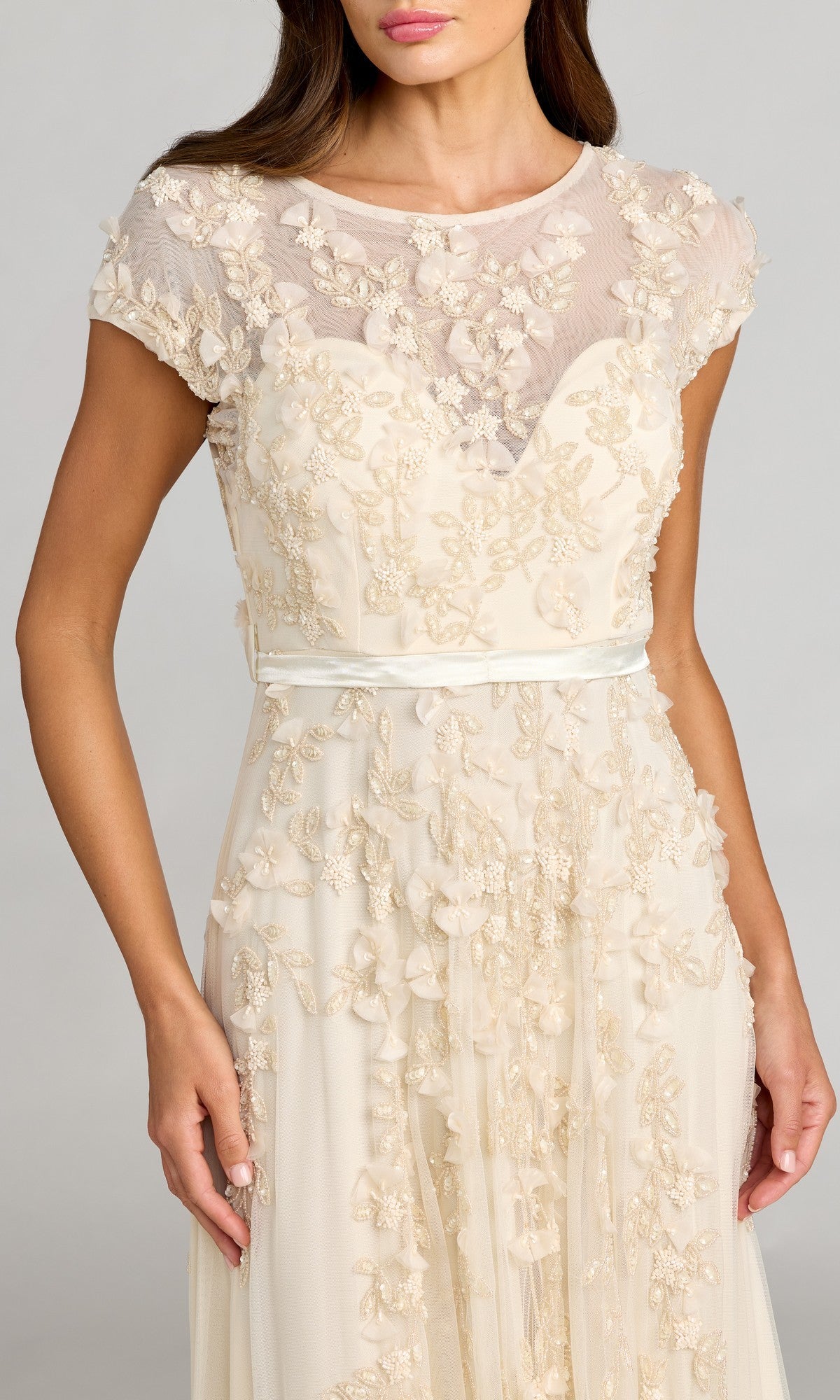 Woman wearing a cream Mac Duggal 14521 cap-sleeve long formal dress with floral embroidery, sheer upper bodice, and satin waistband—a perfect choice for special occasions.