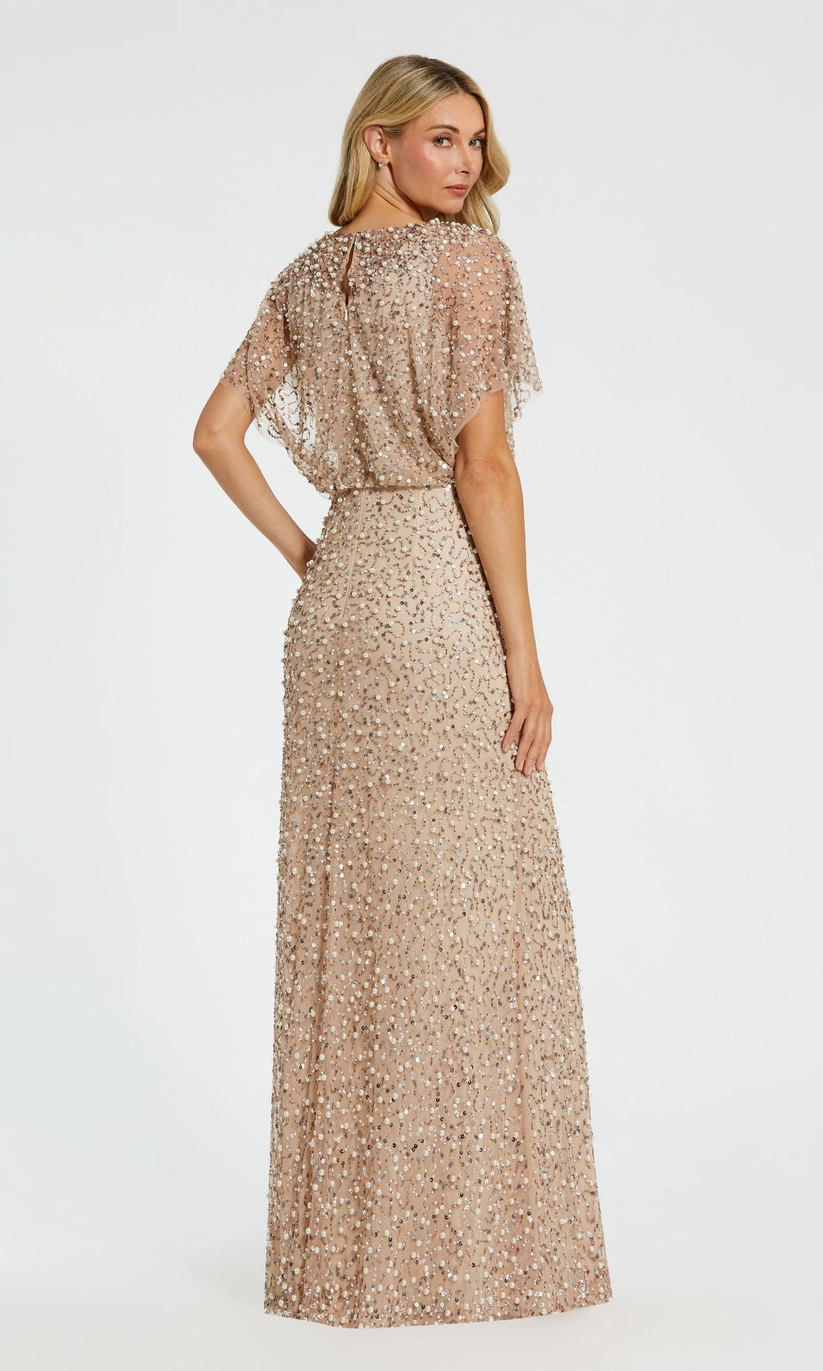 A woman poses with her back turned and head over her shoulder in a Mac Duggal 14523 Beaded Long Nude Evening Gown with short sleeves.