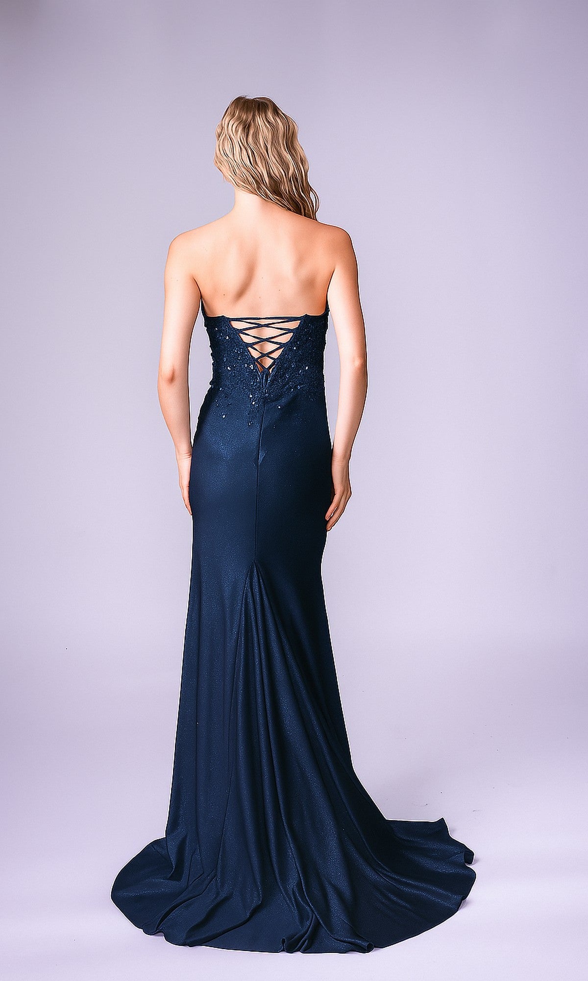 A woman faces away, wearing the Long Formal Dress: Nina Canacci 1607— a floor-length, strapless gown with a lace-up back—ideal for special occasions, set against a plain light purple background.
