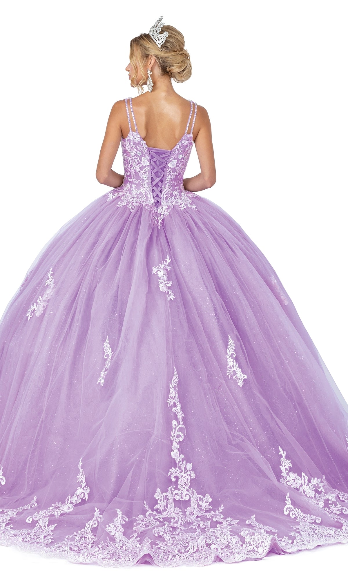 A woman in Quinceanera Dress 1608 By Dancing Queen, featuring a tiara, lavender color, white lace embroidery, lace-up back, and full embellished skirt, stands facing away to showcase the gown’s elegant details.