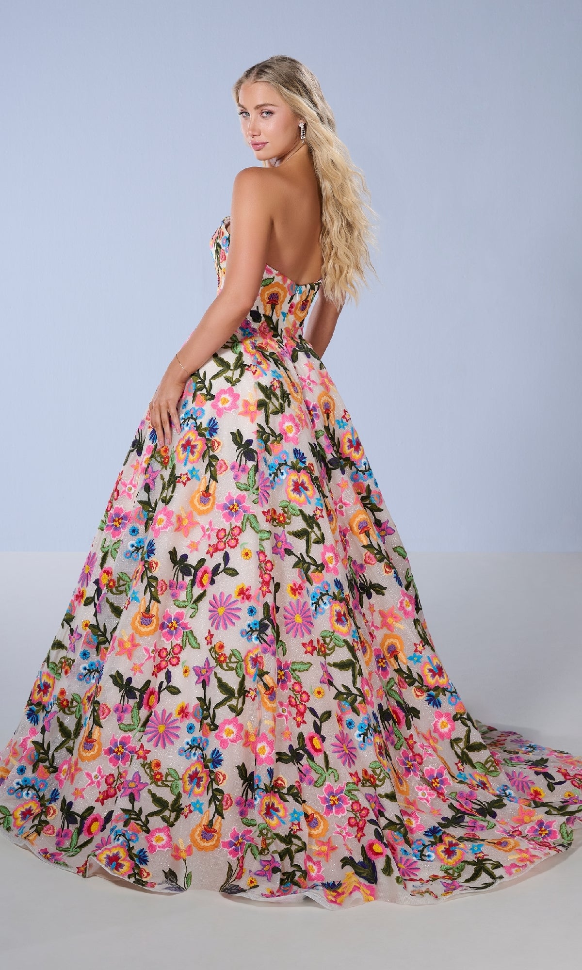 A woman faces away in the Tiffany 16176 Floral Embroidered Prom Ball Gown, showcasing a strapless sweetheart neckline, embroidered floral print, and long flowing train against a plain light blue background.