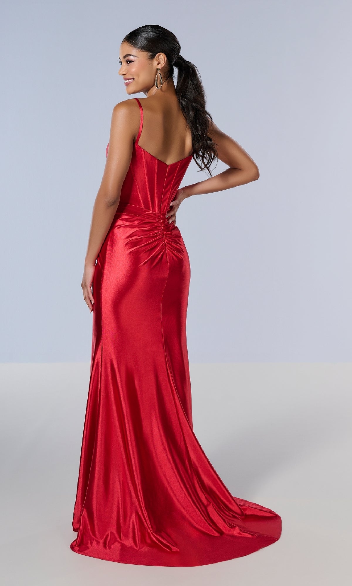 Woman in the Tiffany 16177 long fitted red satin prom dress, featuring a sweetheart neckline and ruched back detail, stands on a plain light background facing away from the camera.