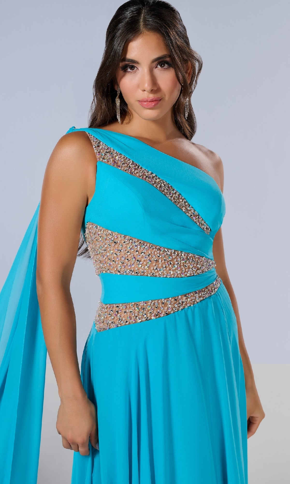 A woman models the Tiffany 16217 long prom dress in bright blue, featuring a one-shoulder design, beaded embellishments, and sheer panel details, standing against a neutral background.
