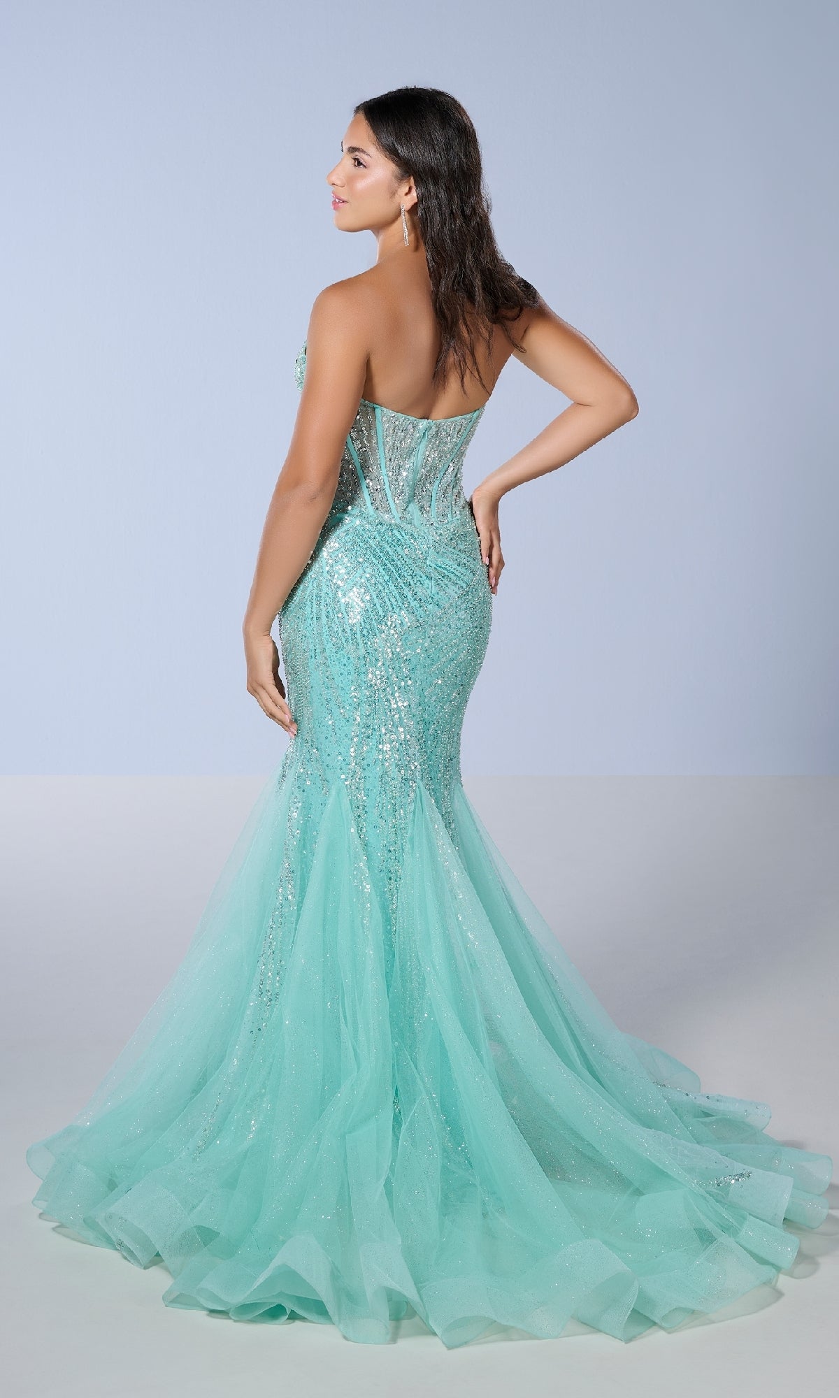 A woman faces away, wearing the Tiffany 16232 long prom dress—a strapless aqua blue mermaid style with a fitted bodice, sequin-embellished tulle skirt, and subtle sweetheart neckline—set against a plain light background.