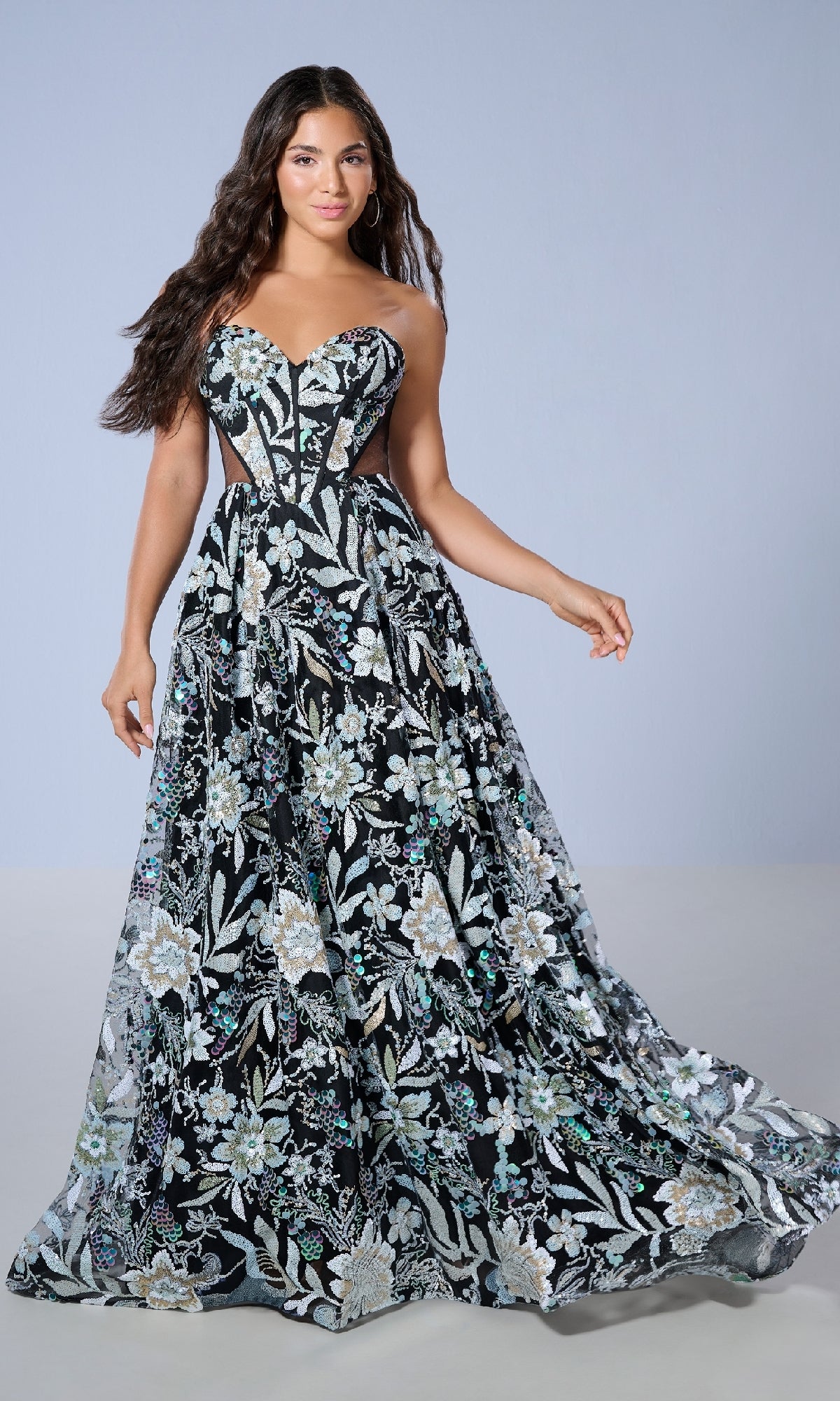 A woman wearing the Tiffany 16238 long prom dress, featuring a strapless floral design and sweetheart neckline, stands against a plain light background, looking at the camera.