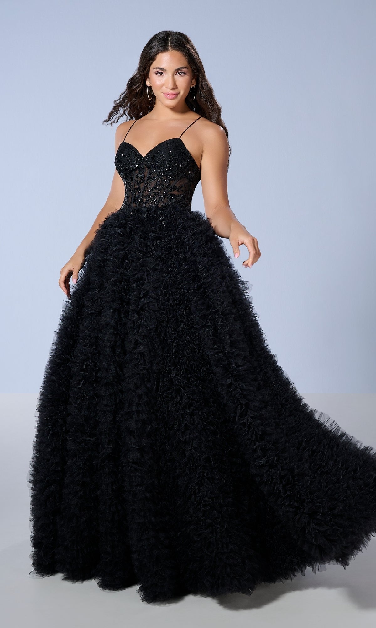 A woman stands in front of a plain light gray background wearing the Tiffany 16252 Long Prom Dress, featuring a black fitted corset bodice and a voluminous textured skirt.