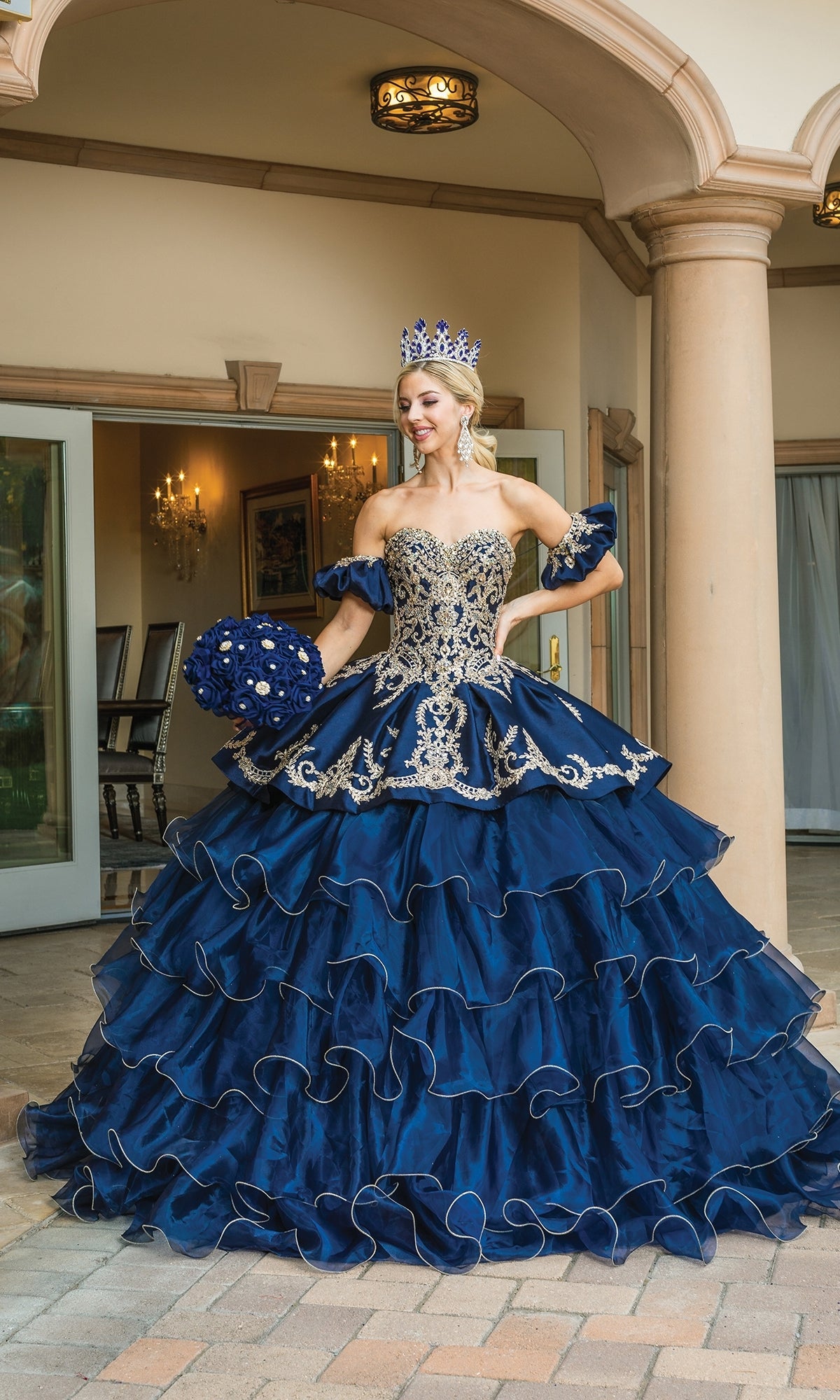 A woman wears the Navy Blue Quinceanera Dress 1637, featuring a ruffle layered skirt.