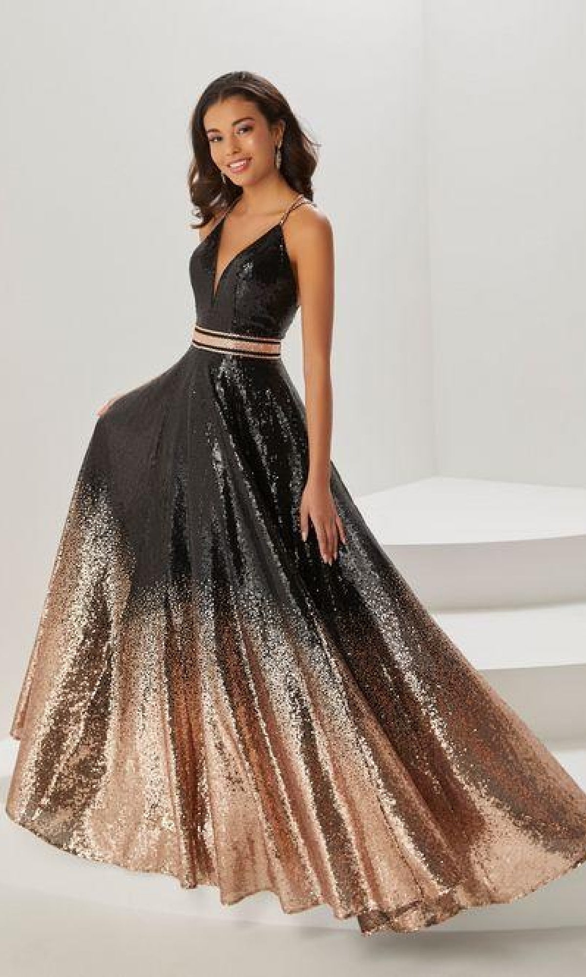 A woman stands in a room wearing the A-Line Sequin Ombre Prom Dress: Tiffany 16941, featuring a low v-neckline and an elegant floor-length skirt.