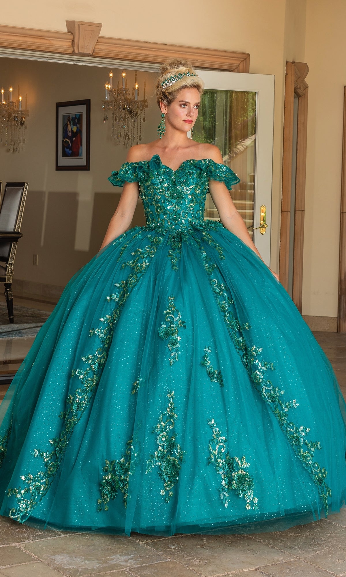A woman stands indoors near an open glass door wearing the Quinceanera Dress 1766 By Dancing Queen, an off-the-shoulder hunter green gown with floral embellishments.