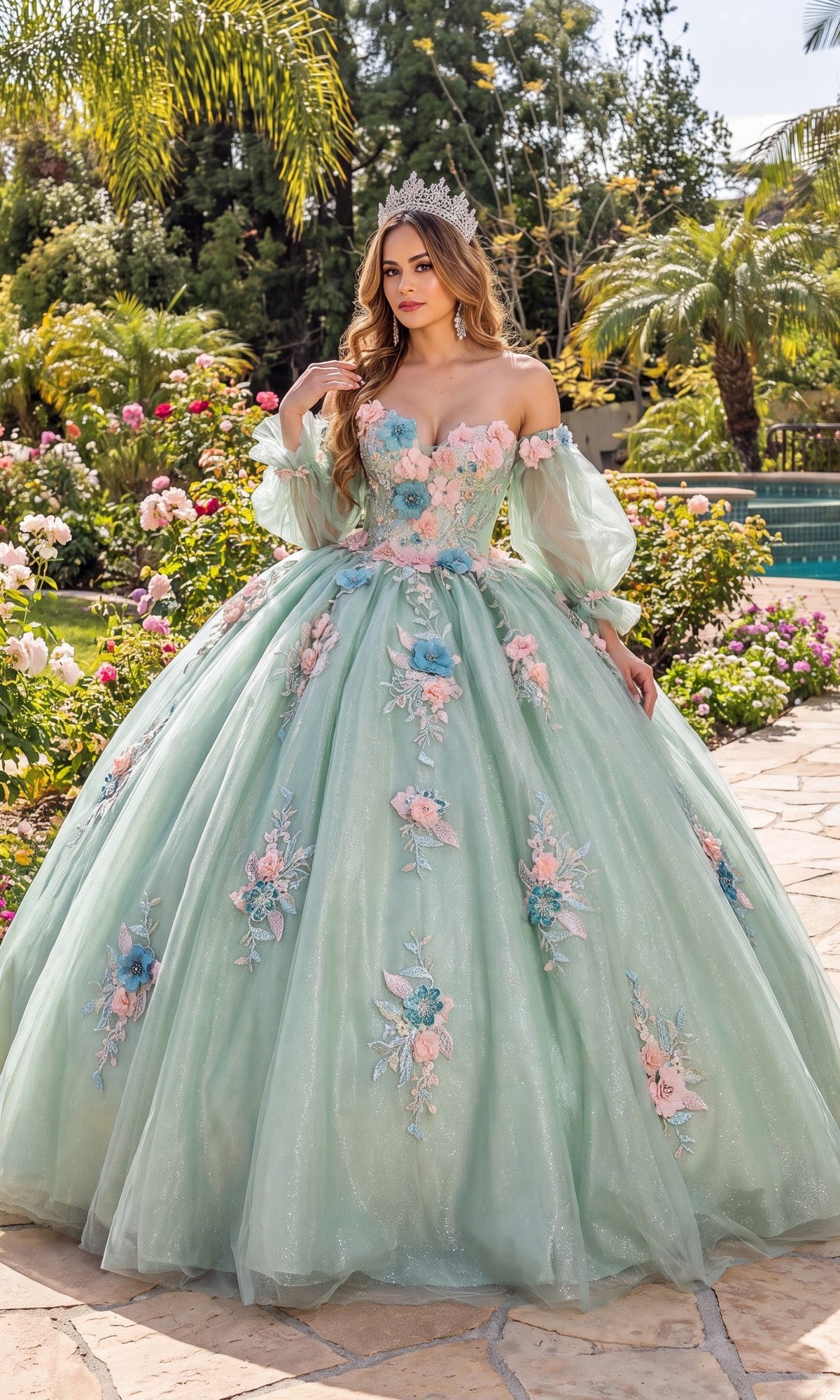 A woman wearing the Quinceanera Dress 1837 By Dancing Queen in sage, featuring a sweetheart neckline and delicate floral appliqués, stands crowned on a garden path surrounded by flowers and palm trees.
