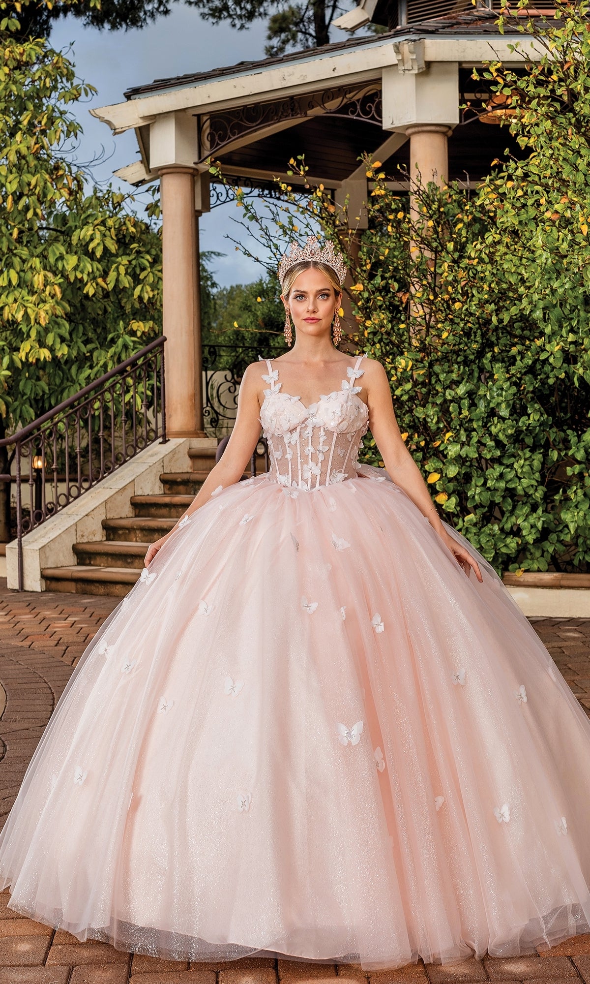 A woman in a luxurious pink quinceañera a-line ball gown with sweetheart neckline and bow detail on the back, standing in an elegant room.
