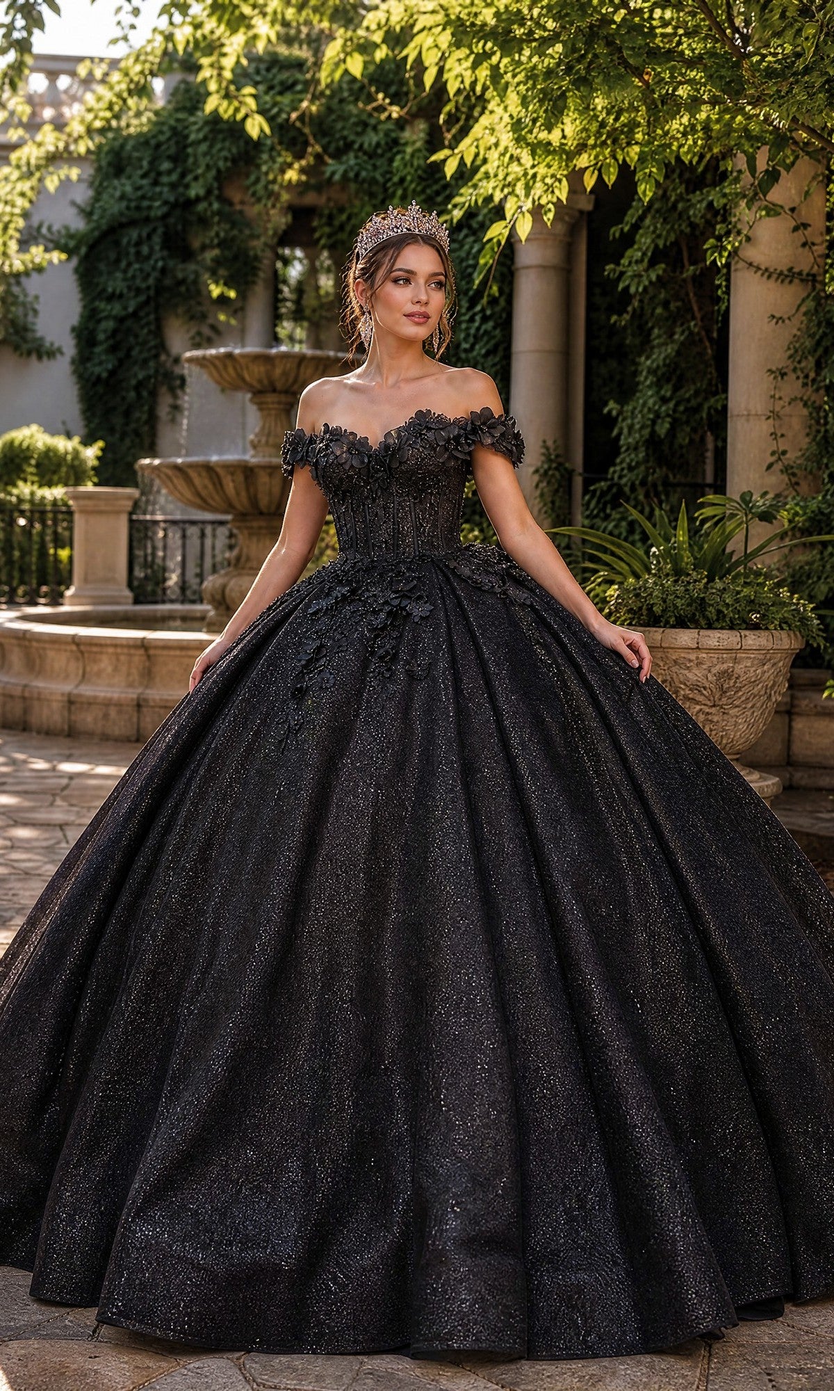 A woman wearing the Quinceanera Dress 1888 By Dancing Queen in black, along with a tiara, stands outdoors near a fountain and greenery, posing for a photo.