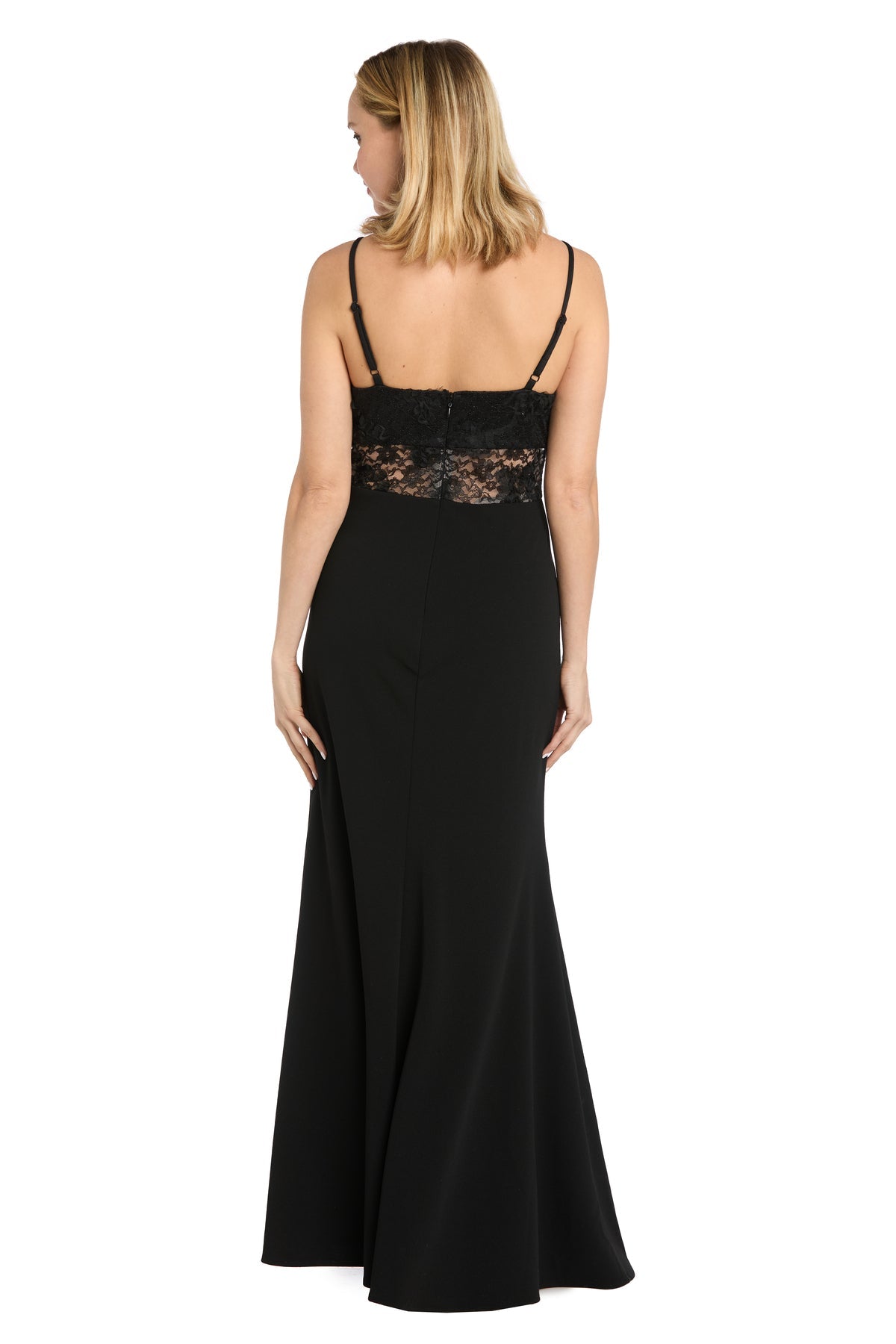 A woman stands with her back to the camera, wearing the Morgan 19084M Sheer-Lace Corset Prom Dress—long, black, with thin straps and an illusion lace corset panel on the upper back—set against a white background.