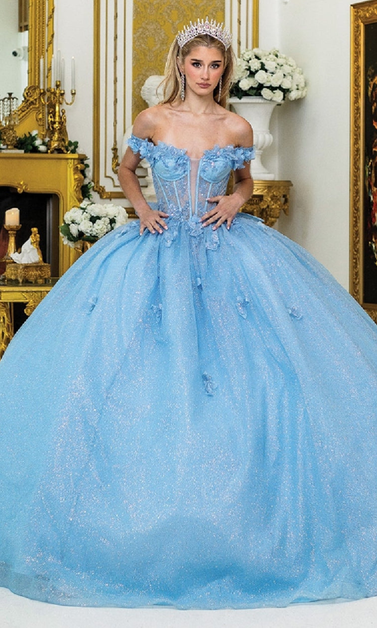 A woman in the Quinceanera Dress 1933 By Dancing Queen, featuring sparkling light blue off-the-shoulder fabric and a tiara, stands in a lavish room adorned with gold accents and white flowers.