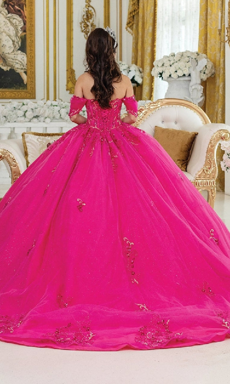 A woman with long brown hair, seen from behind, sits on an ornate cream and gold sofa in an elegant room wearing the Pink Quinceanera Dress 1987 By Dancing Queen, featuring fuchsia pink fabric with gold details and a corset bodice.
