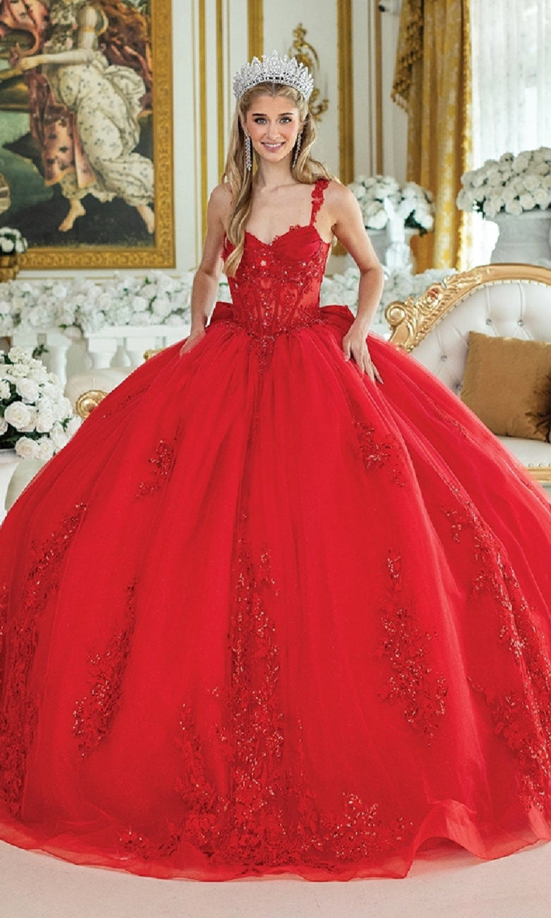 A woman in the Quinceanera Dress 1989 by Dancing Queen, a voluminous red gown with floral embellishments and a jeweled crown, stands in an ornate room adorned with white flowers.