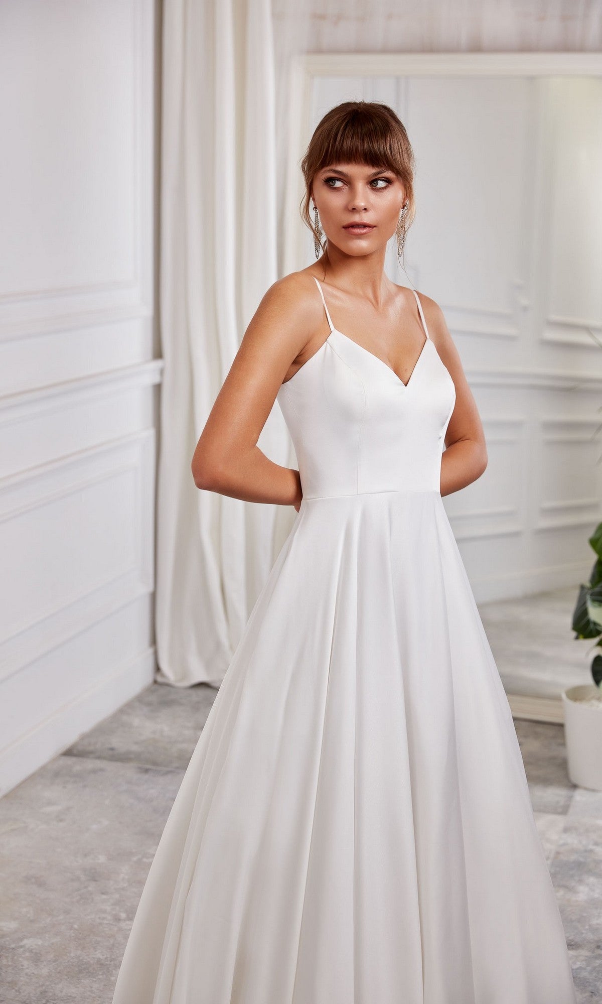 A woman in the Long White Dress: Aerie Couture 2000, featuring an a-line skirt, stands indoors in a light-colored room, looking to her side.