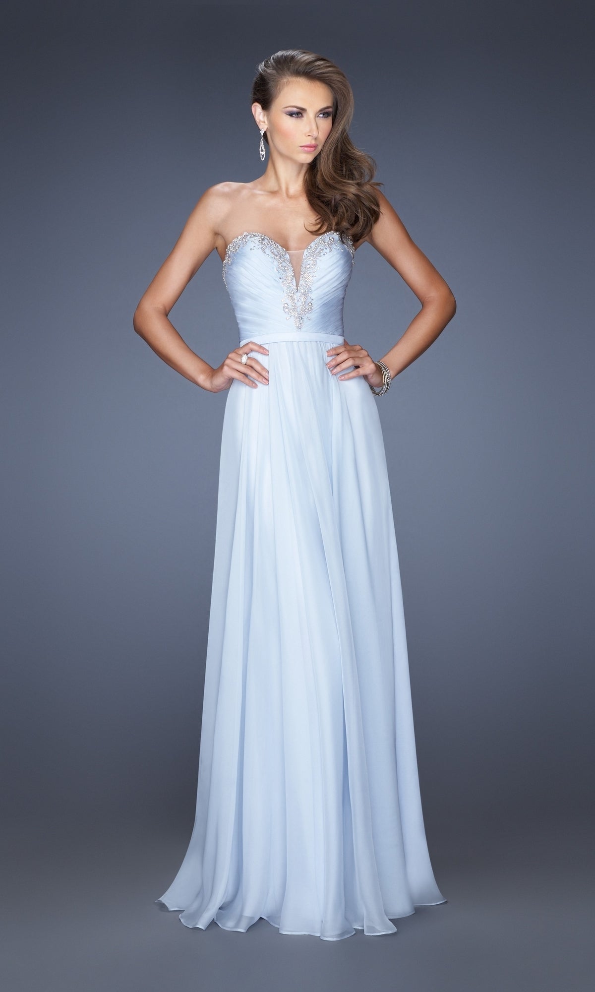 A woman models the La Femme Designer Pleated Chiffon Prom Dress 20027—a floor-length, light blue strapless gown with a sweetheart neckline and silver accents—standing against a plain grey background.