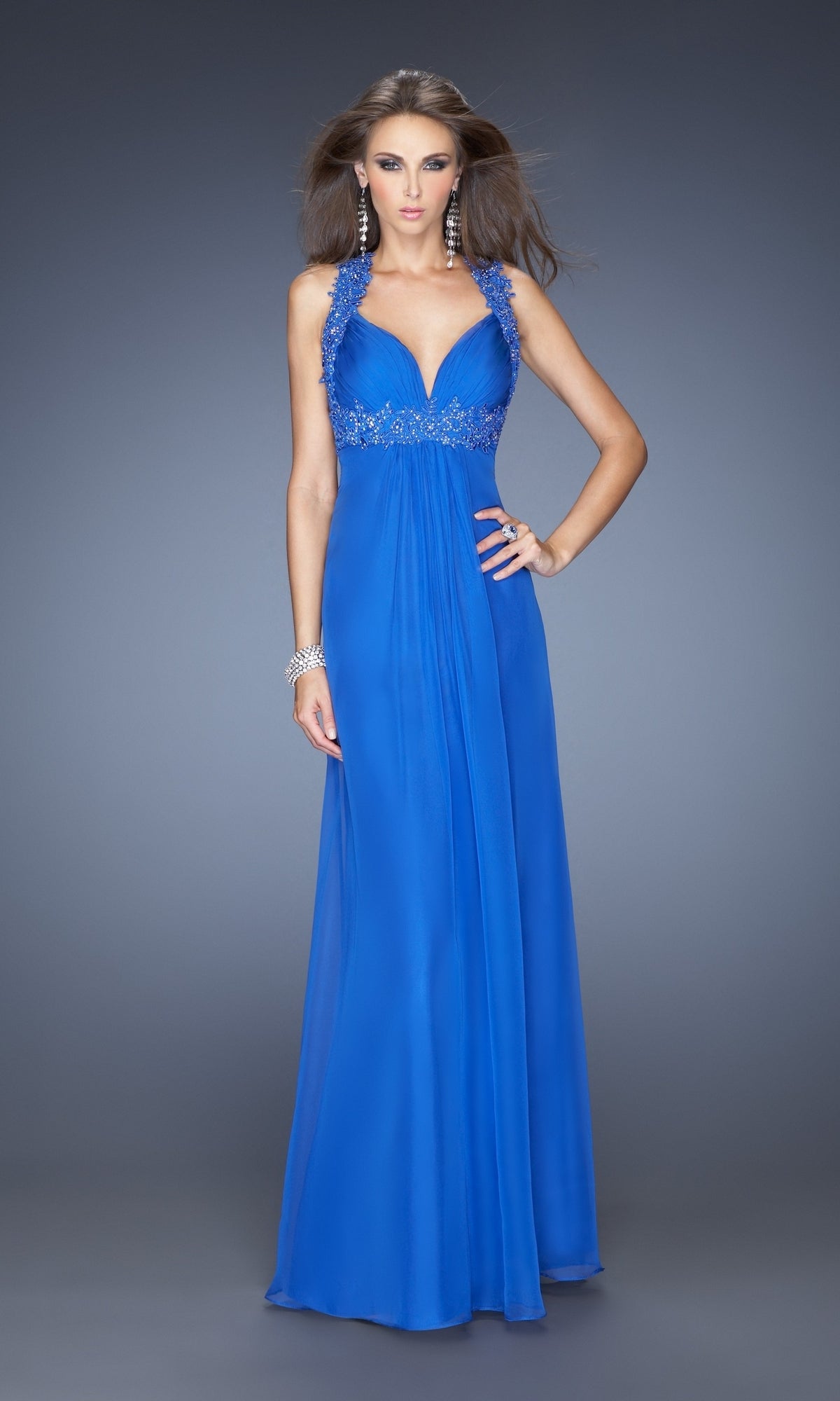A woman models the La Femme Empire-Waist Ruched Chiffon Prom Dress 20134, a floor-length royal blue gown with beaded details, a sleeveless cut, and an elegant open back, posing against a gray background.