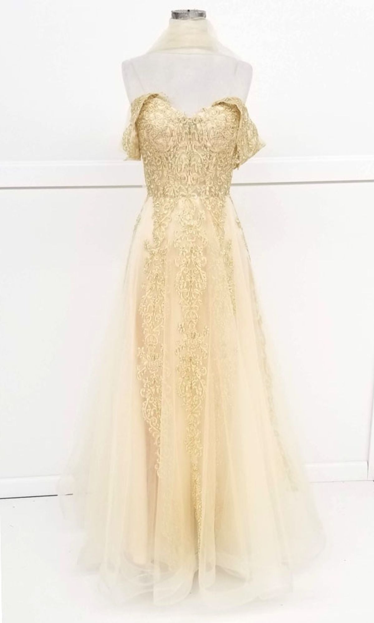 The Long Lace Prom Ball Gown: Chicas CA1103 features a cream-colored, off-the-shoulder lace bodice with gold detailing and a flowing tulle skirt, elegantly showcased on a dress form against a white background.