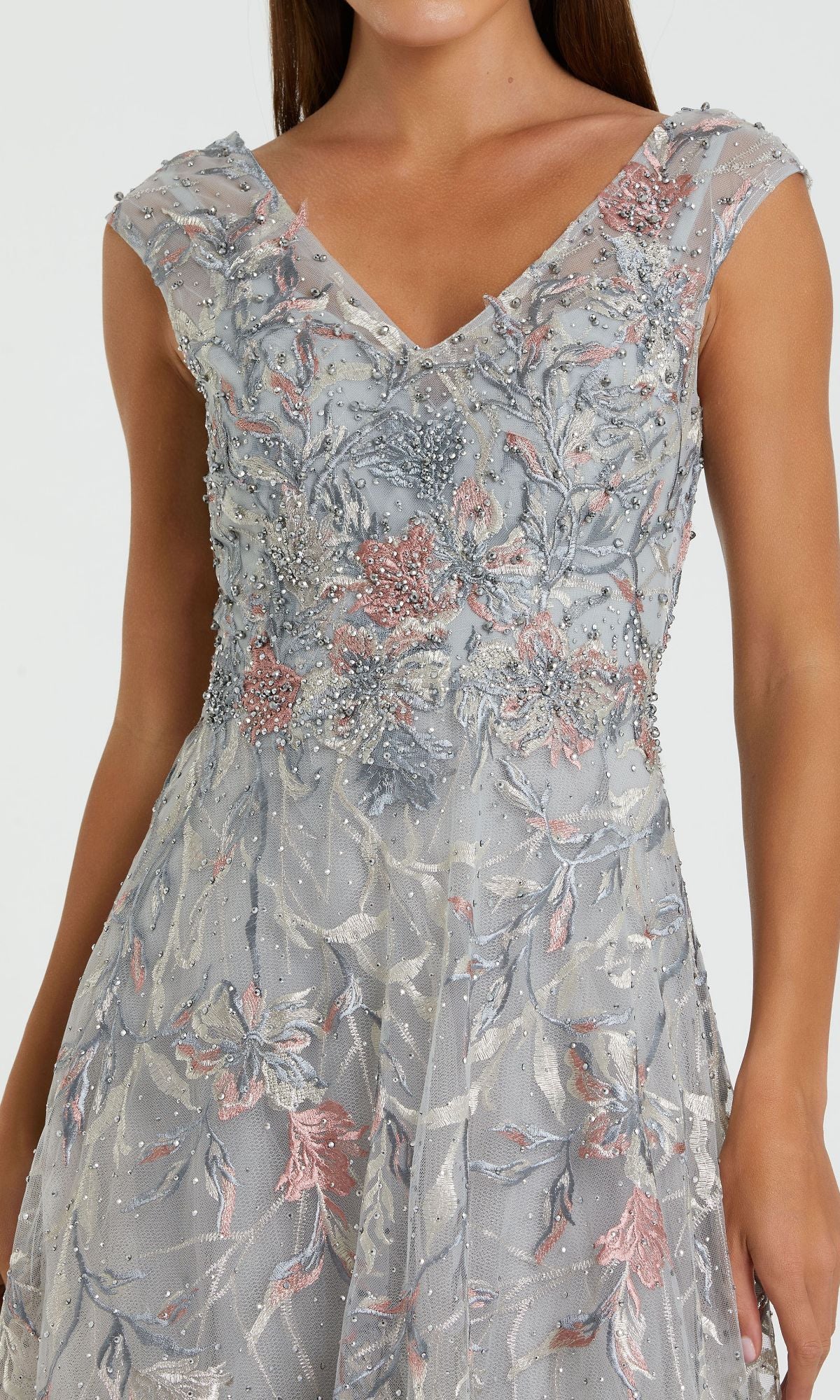 A woman wears the Cap-Sleeve Long Print Prom Dress (Mac Duggal 20263), featuring cap sleeves, an A-line silhouette, and intricate silver and blush floral prints on sheer fabric.