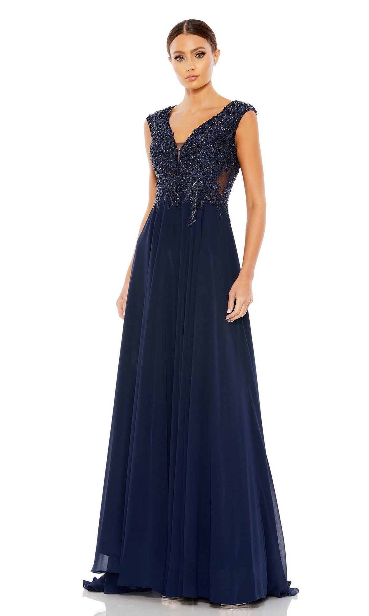 A woman models the Mac Duggal 20264 Beaded-Bodice Long Formal Dress, featuring a navy blue A-line silhouette, beaded V-neck bodice, and cap sleeves, standing against a plain white background.