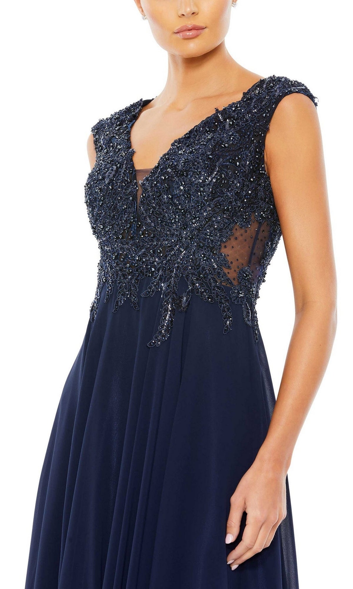 A woman wears the Beaded-Bodice Long Formal Dress by Mac Duggal 20264, a sleeveless navy blue evening gown with a beaded v-neck bodice and sheer mesh side panels.