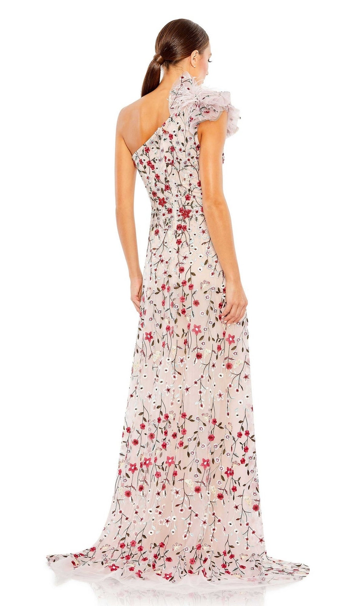 A woman stands facing away, hair in a low ponytail, wearing the Mac Duggal 20331 One-Shoulder Print Formal Gown featuring a long floral design and ruffled sleeve.