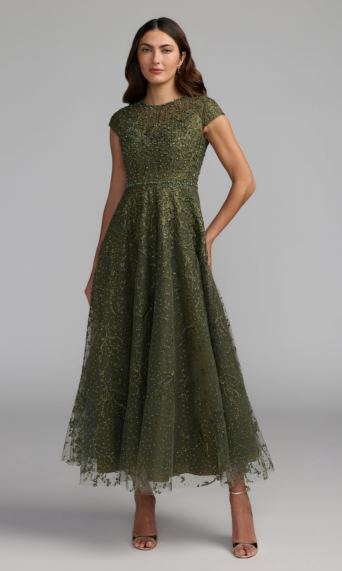 Woman wearing an olive Tea Length Lilac Party Dress, style Mac Duggal 20338, featuring cap sleeves and intricate beaded embroidery, posing against a plain gray background.