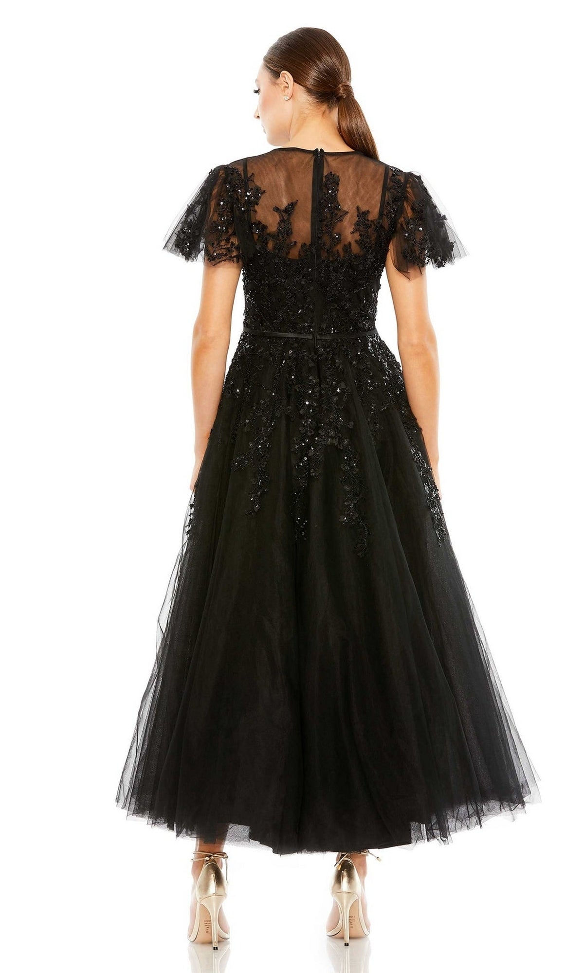 A woman with a ponytail is seen from behind wearing the Long Formal Dress 20362 by Mac Duggal—a black, tea-length, short-sleeved A-line dress featuring sheer tulle, floral embroidery, and beige high heels.