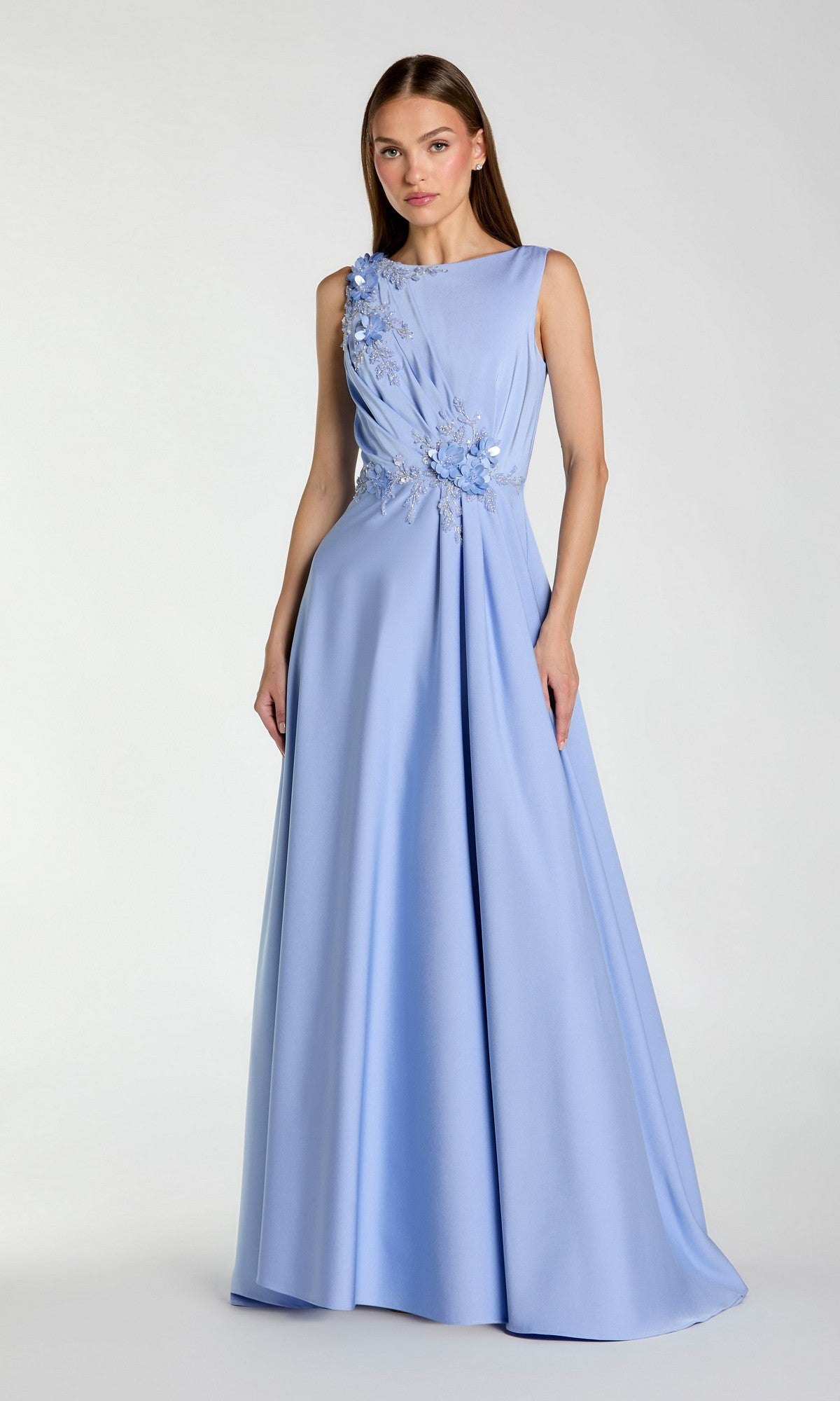 A woman wears the Mac Duggal 20365 sleeveless long formal dress, featuring a floor-length light blue skirt and beaded floral embroidery on the bodice, standing against a plain light background.