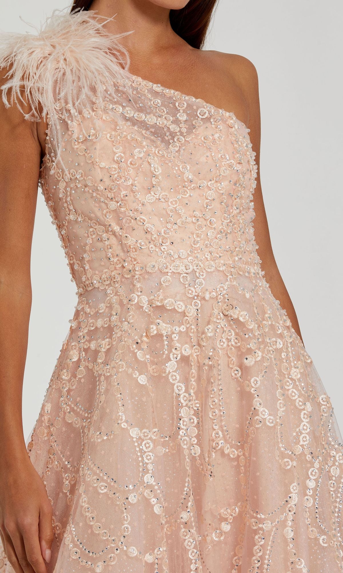 A woman in the Mac Duggal 20389 Beaded One-Shoulder Prom Gown, light pink with sequins and a feathered shoulder detail.