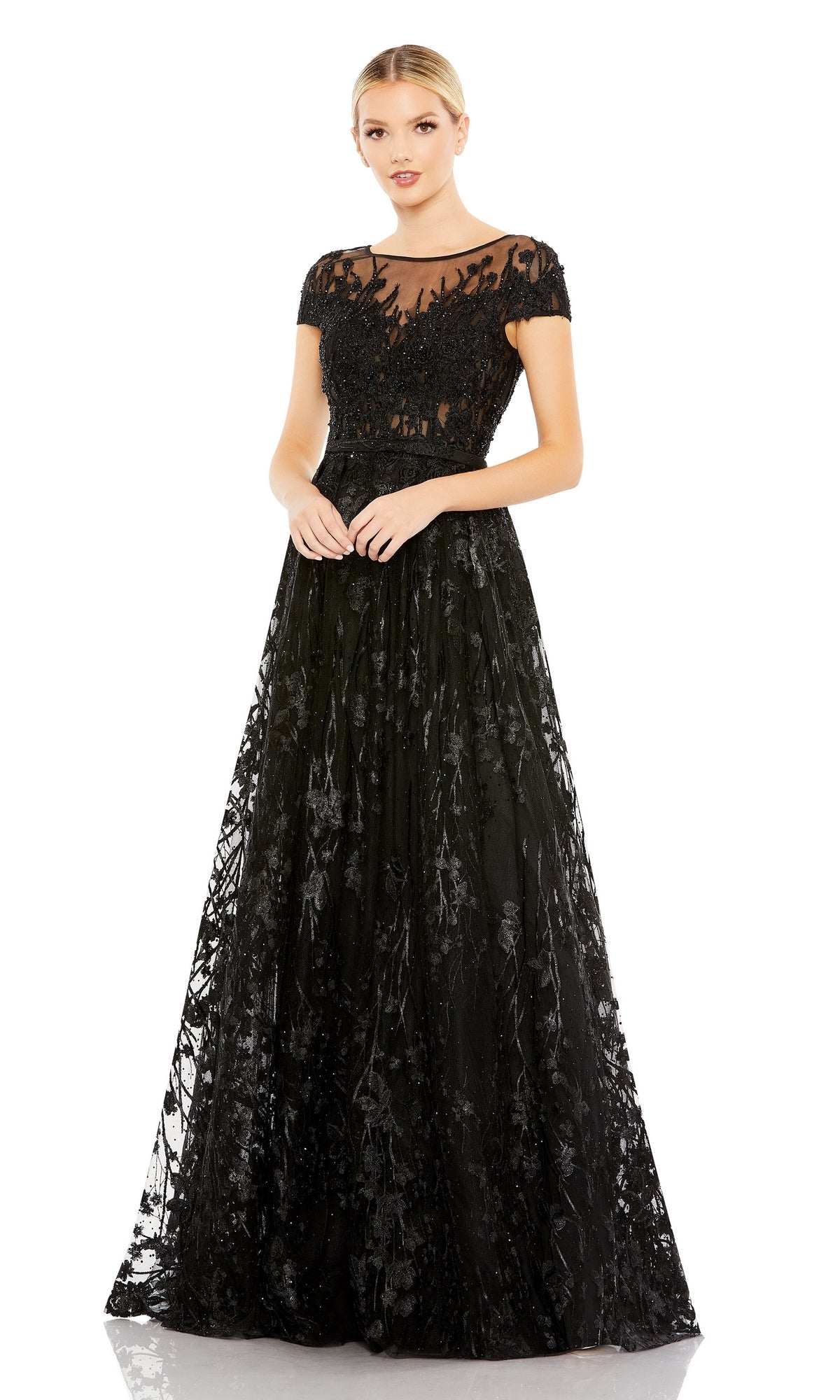 A woman stands against a plain white background wearing the Mac Duggal 20405, a short-sleeve long formal dress featuring lace, a sheer neckline, and floral detailing.