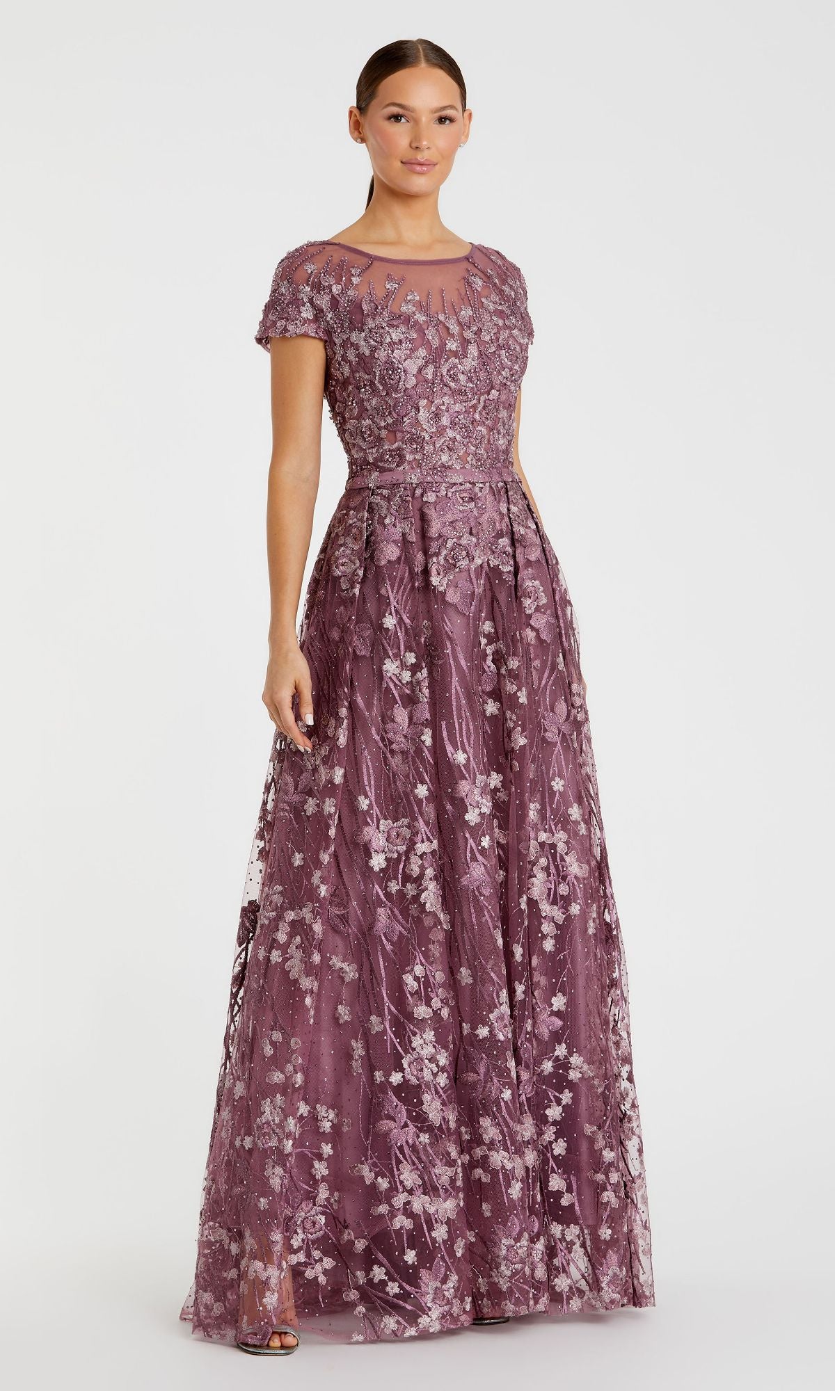 Wearing the Mac Duggal 20405 Short-Sleeve Long Formal Dress with floral embroidery and a sheer neckline, a woman stands against a plain white background.