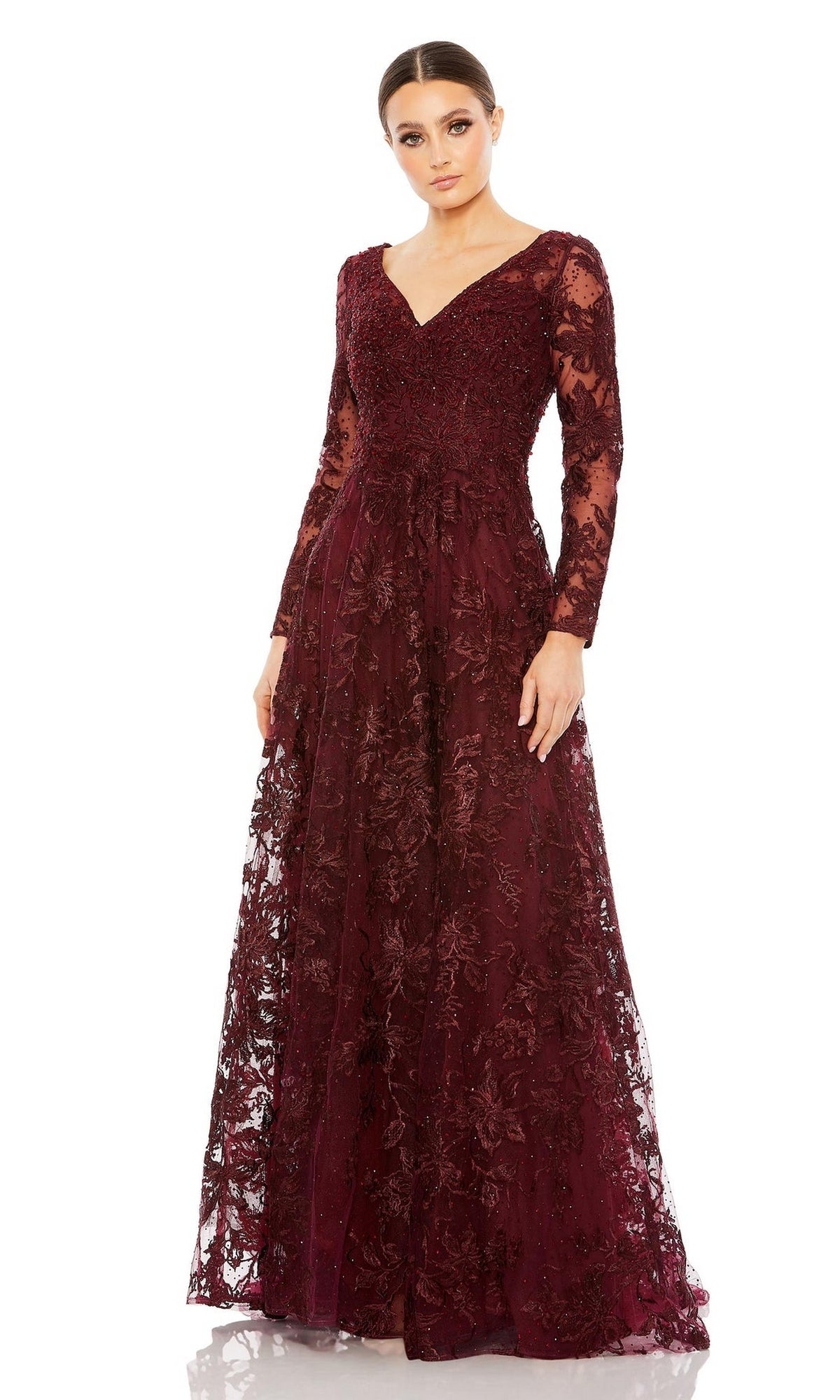 Woman wearing the Mac Duggal 20409 long formal dress in mahogany, featuring floor-length lace embroidery, floral details, long sleeves, and a v-neckline, standing against a white background.