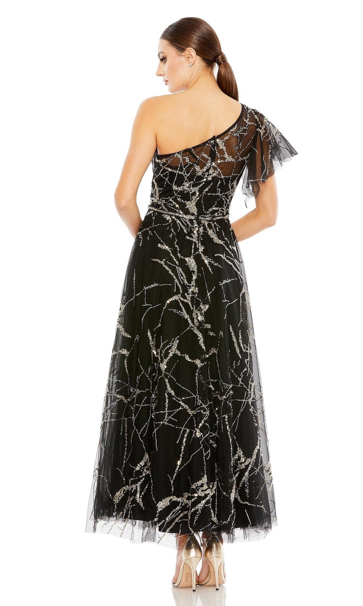 A woman faces away wearing the Long Formal Dress 20427 by Mac Duggal, featuring a black one-shoulder A-line silhouette with silver branch patterns and tulle overlay, paired with beige high heels.