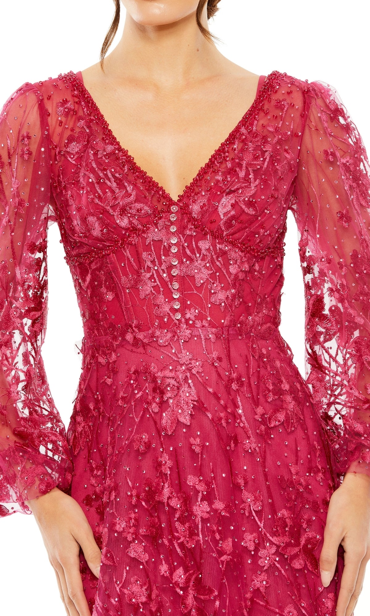A woman wears the Mac Duggal 20430, a deep pink long-sleeve formal dress featuring a V-neck lace design, bead and floral embroidery, and button details on the bodice.