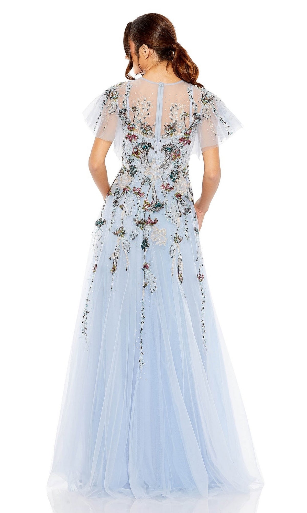 A woman stands facing away from the camera in the Mac Duggal Long Formal Dress 20436, a light blue, floor-length A-line gown featuring embroidery, flutter sleeves, and floral details.