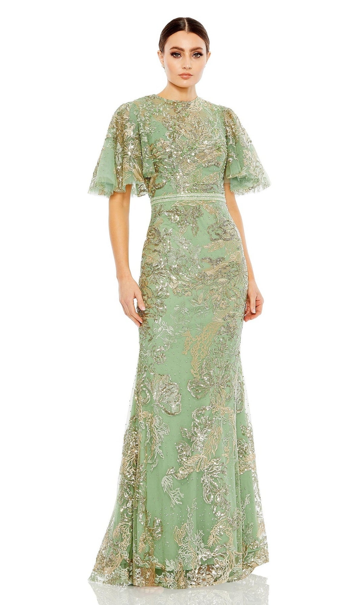 A woman wears the Mac Duggal 20438 Flutter-Sleeve Lace Formal Dress—floor-length, light green with gold embroidery, sparkly lace, and short flared sleeves—standing against a white background.