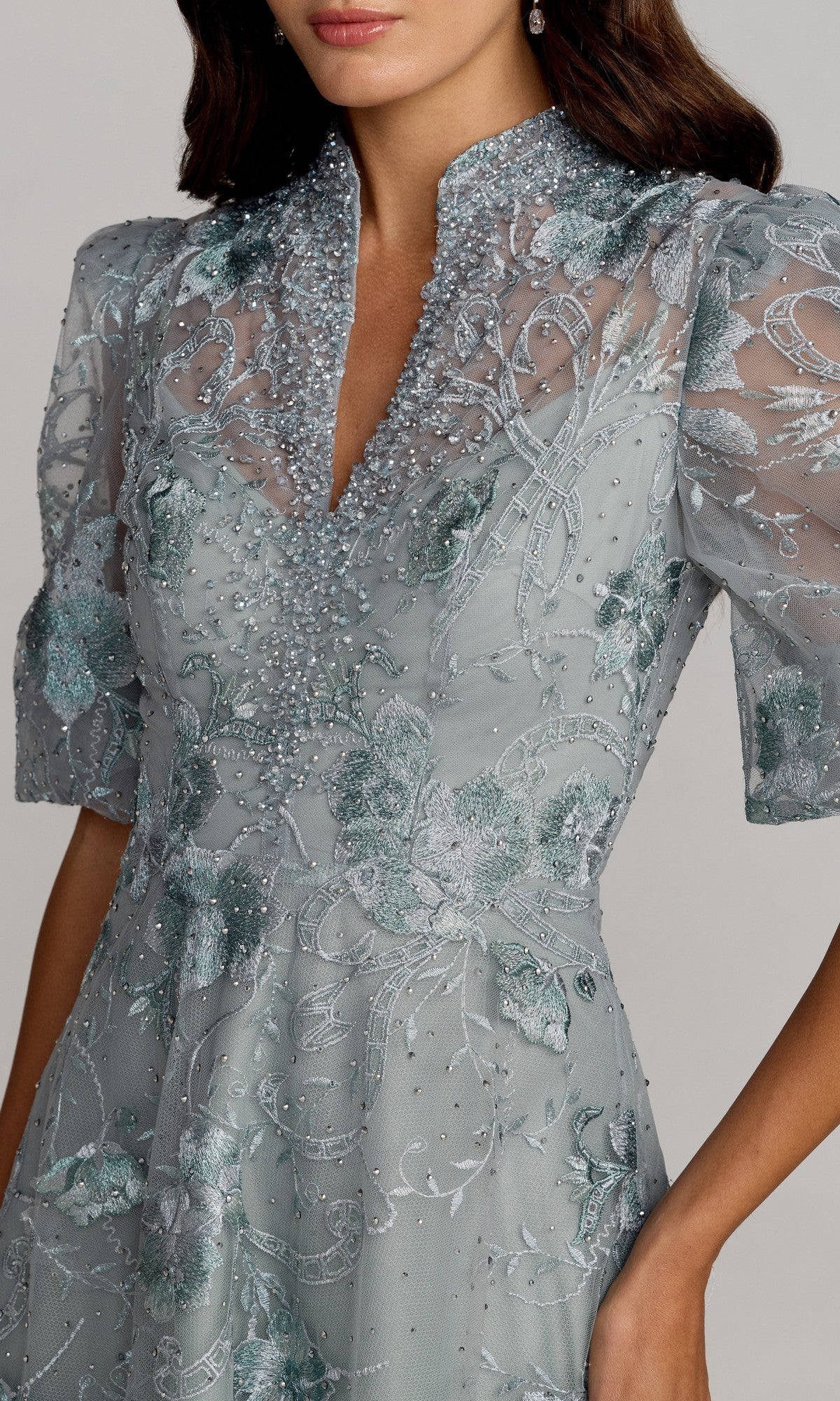 A woman wearing the Mac Duggal 20452 Short Sleeve Beaded Formal Gown in light blue with floral embroidery and a high collar, her face partially out of frame.