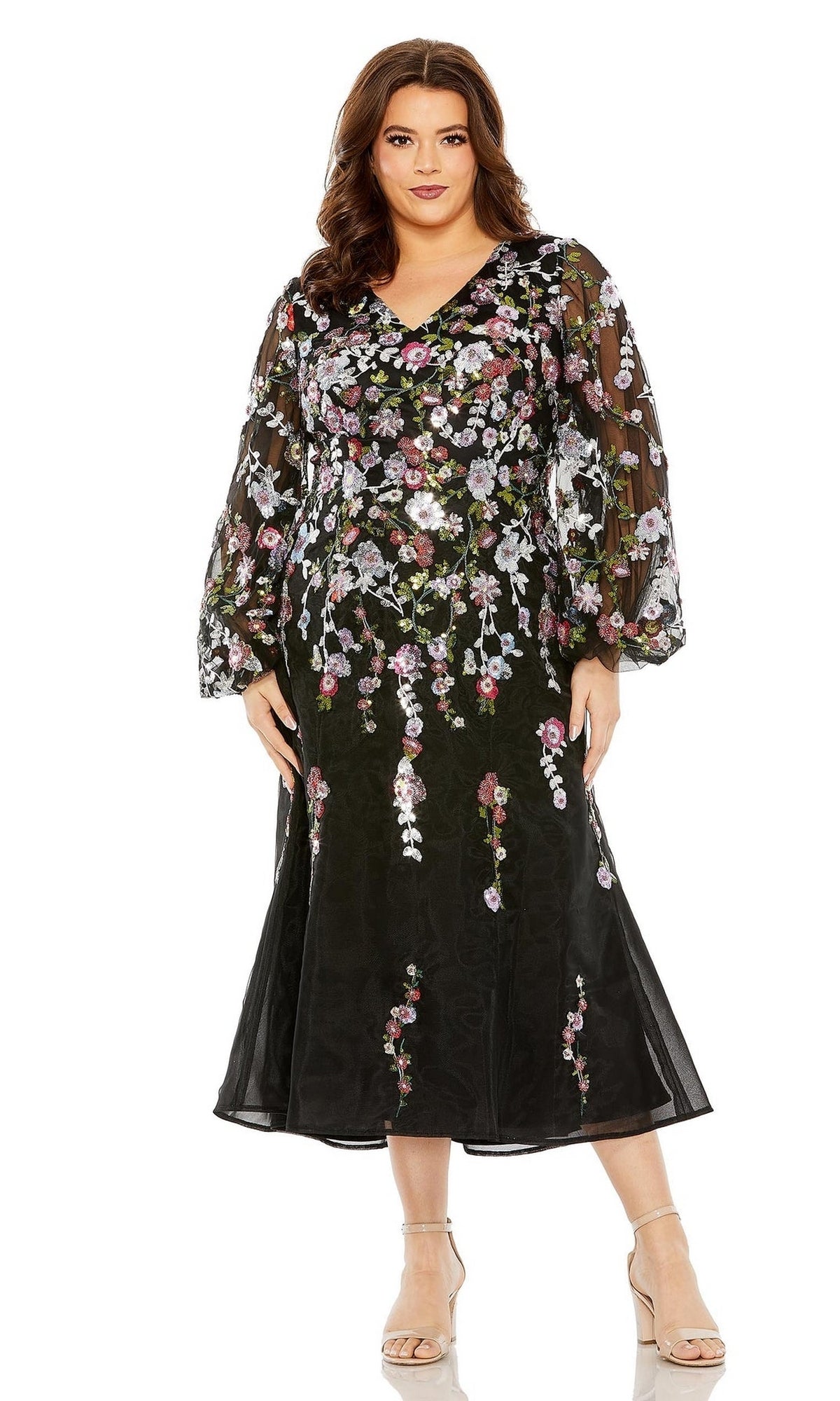 A woman stands facing forward in the Plus-Size Semi-Formal Dress 20474 by Mac Duggal, a black midi dress with sheer long sleeves and floral embroidery, paired with nude heels for a chic look.