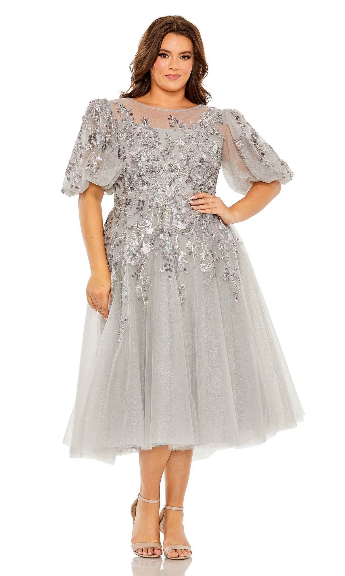 A woman wears the Plus-Size Semi-Formal Dress 20475 by Mac Duggal—an elegant knee-length, embroidered midi A-line dress with floral details and short puff sleeves, paired with strappy sandals, perfect for any special occasion.