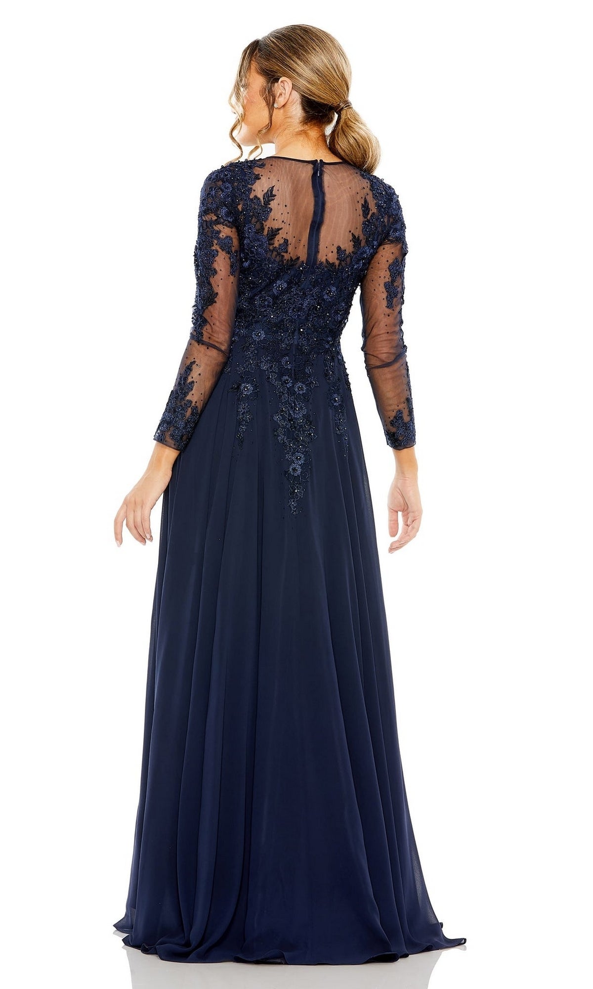 A woman stands facing away, wearing the Mac Duggal 20478 long sleeve long formal dress in navy blue, featuring an A-line silhouette, sheer sleeves, floral lace embroidered bodice, and a keyhole back.