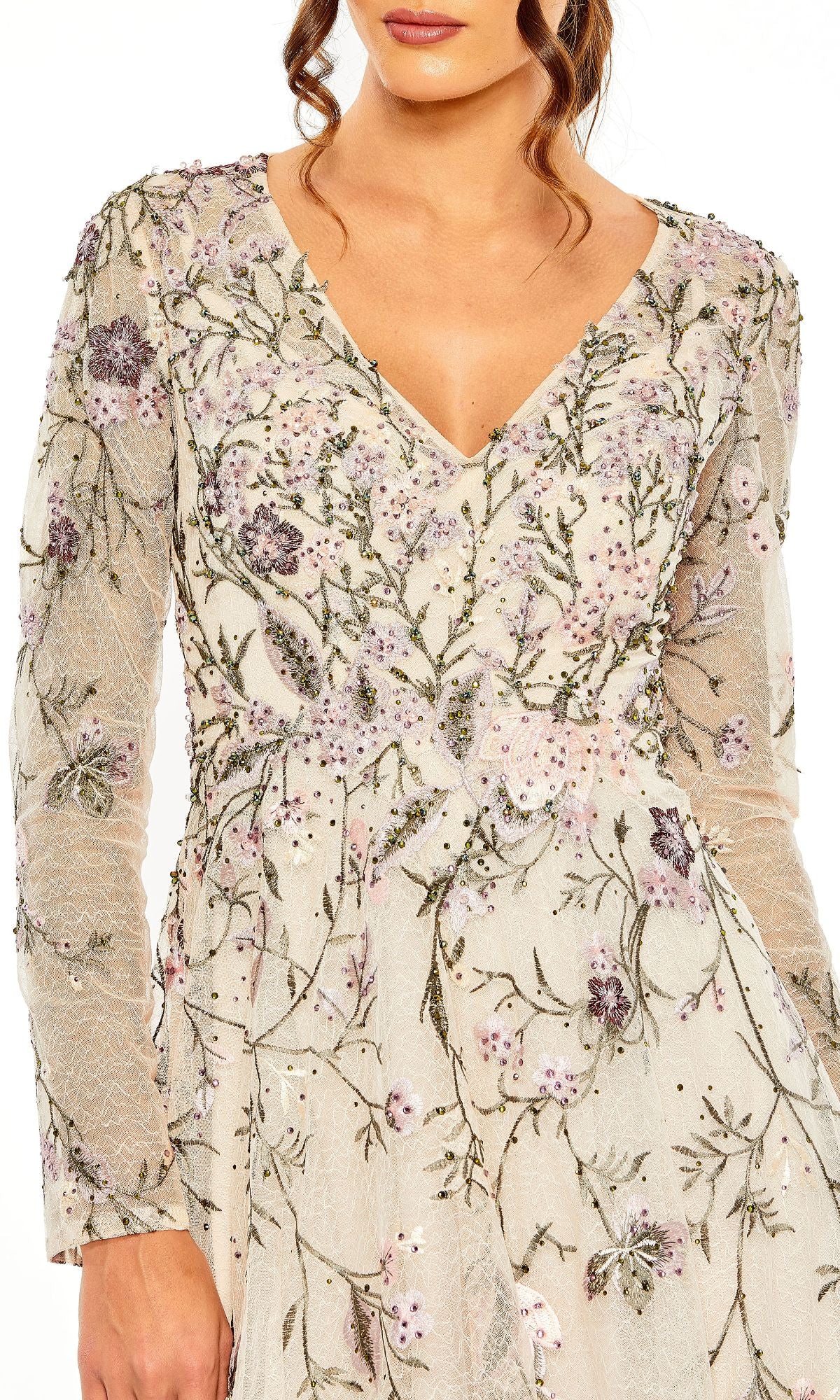 A woman wears the Mac Duggal 20480, a long-sleeve pink evening gown with a V-neck and delicate floral embroidery on sheer fabric.